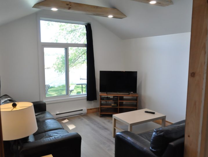 Living room with TV and large window overlooking White Lake at The Cove 245B cottage rental.